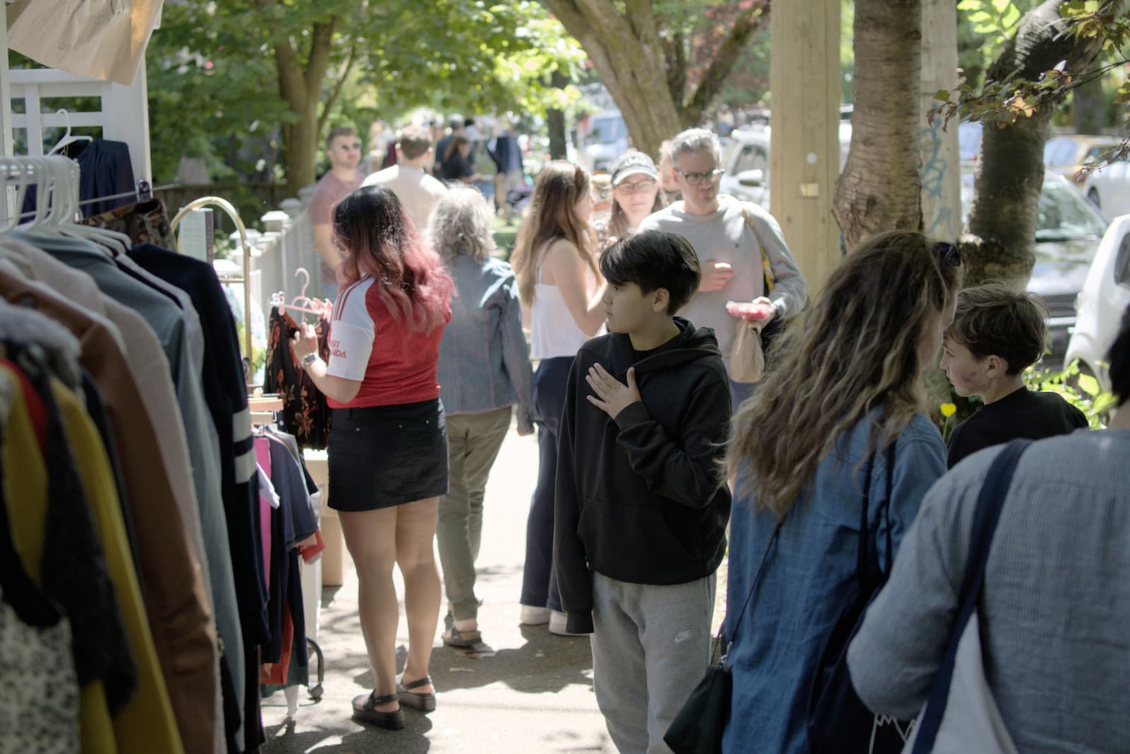 Shoppers browsing clothing racks and tables along a tree-lined street during the May 30 Kitsilano Yard Sale Walk.